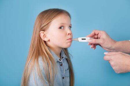 Cute little ill girl with a electronic thermometer on blue backgroundの写真素材