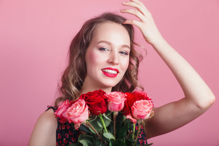 Happy laughing romantic woman holding flowers on pink background. Beauty woman with rosesの写真素材