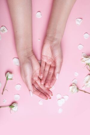 Elegant and graceful hands with slender graceful fingers is touching to each other on pink background with flowersの写真素材