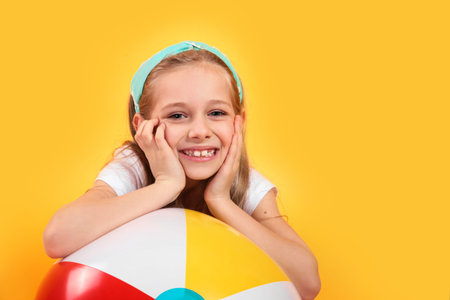 Portrait of funny happy child in summer clothes with beachball on yellow background