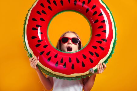 cute surprised girl in red sunglasses looking through floating ring on yellow studio backgroundの写真素材