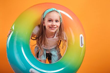 Portrait of a cheerful beautiful little girl looking through an inflatablering on yellow background,の写真素材
