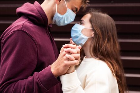 Couple in quarantine trying to kiss wearing a mask outdoor . Focus on handsの写真素材