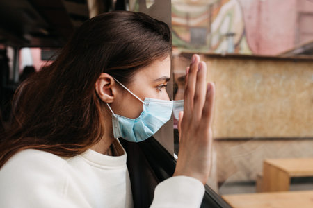 Sad woman looking in window in isolation at home for virus outbreak or hypochondria .