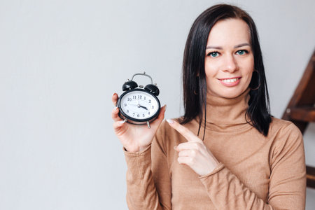 Close-up portrait of beautiful girl looking at you and holding an alarm clock in her hand, Time-managementの写真素材