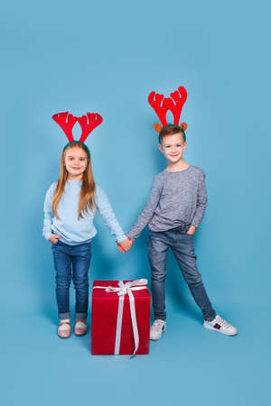 happy funny emotional children boy and girl in red Christmas reindeer costume holding big red giftの写真素材