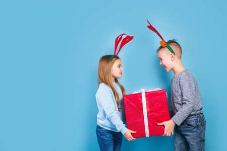 happy funny emotional children boy and girl in red Christmas reindeer costume holding big red giftの写真素材