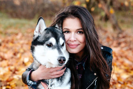Portrait of smiling brunette woman and her husky dog in autumn park.の写真素材