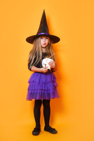 Laughing funny child girl in a witch costume in halloween on orange background