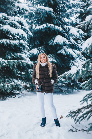 Outdoor portrait of young beautiful fashionable happy smiling girl wearing fur winter coat in forest