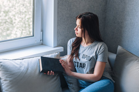 Young woman is reading a book while sitting on a sofa in the living room.