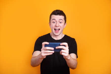 Excited man playing online game on mobile phone on blue backgroundの写真素材