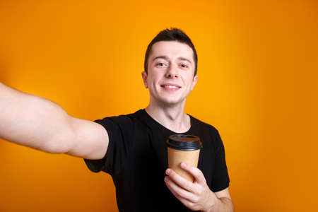 Happy smiling young man making selfie with coffee on yellow background.の写真素材