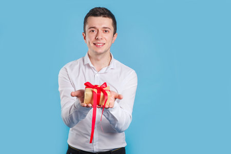 Handsome young excited man holding present gift box on blue background.