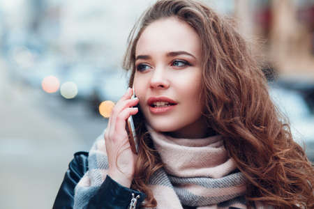 Young woman with coffee talking on mobile phone outdoors in cityの写真素材