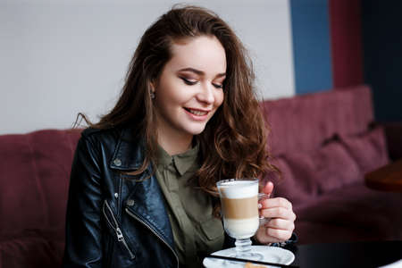 Happy young woman drinking coffee at the cafe, looking downの写真素材