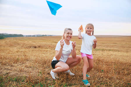 mother and daughter are playing with paper planes and smiling while spending time outdoorsの写真素材