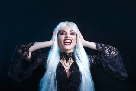 Portrait of vampire smiling creepily before a bite on black background