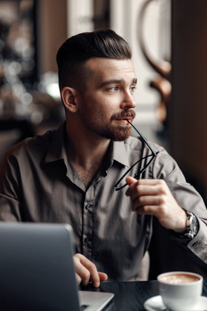 Close-up portrait of businessman with black eyeglasses looking away in cafeの写真素材