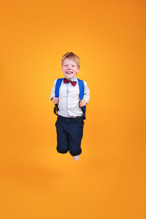 Funny school boy with a backpack jumping on yellow studio backgroundの写真素材