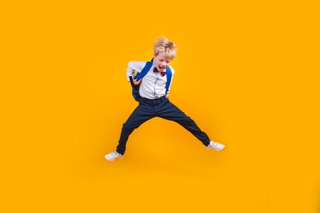 Little school boy student jumpsing high like a super hero on yellow backgroundの写真素材