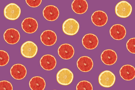 Pattern made of red and yellow grapefruit on vivid purple background. Fresh organic food in vibrant...