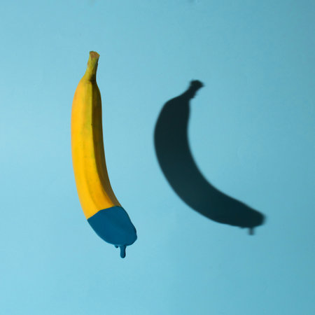 Banana dipped in a dark blue paint on vivid background with hard shadow. Creative concept, minimalist art.の写真素材