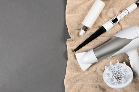 Hairstyling tools (white hairdryer, hairspray, spray, cone curling wand) on beige towel. Top view.の写真素材