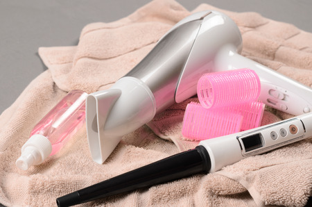 Hair Styling tools (white hairdryer, hairspray, curler, spray, cone curling wand) on beige towelの写真素材
