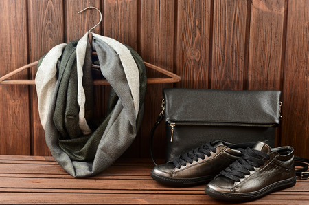 Leather upper metallic womens shoes, scarf and black leather bag on brown wooden background.  Womens leather shoes and accessoriesの写真素材
