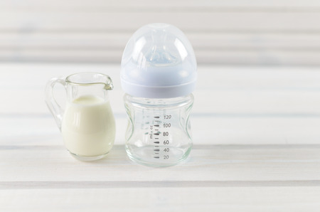 Glass baby bottle and milk jug on white wooden backgroundの写真素材