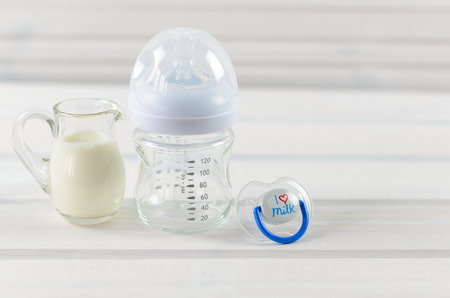 Glass baby bottle, milk jug and baby pacifier on white wooden backgroundの写真素材
