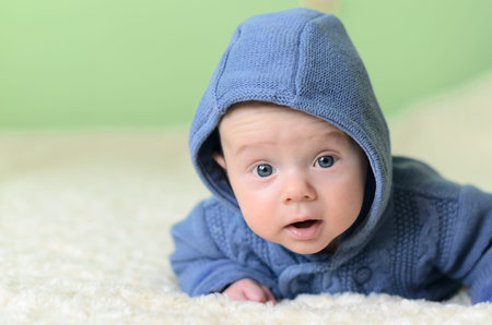 Little boy in blue knitted cardigan lying on stomach and looking at camera