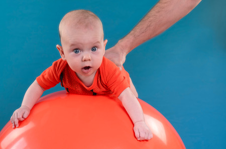 Cute baby lying on the orange fitball on the blue background. Concept of caring for the baby's health.の写真素材