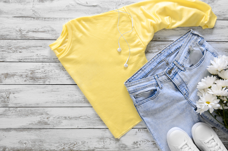 Womens fashion clothing, shoes and accessories (white leather sneakers, blue jeans, yellow top (long sleeve t-shirt) headphones, perfume and fresh flowers.の写真素材