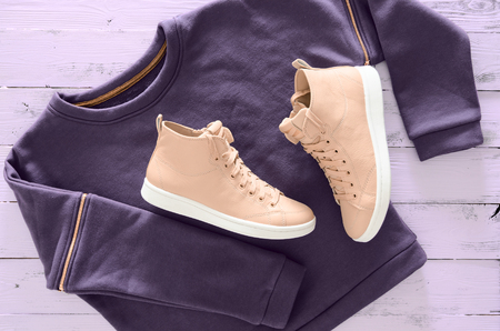 Women clothing, footwear (violet sweatshirt, leather sneakers) on wooden background. Outfit for teens. Top view, flat lay. Trendy colorsの写真素材