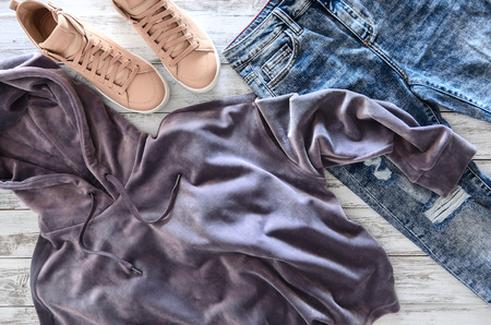 Womens clothing, footwear (violet velvet hoodie, acid washed jeans, leather sneakers) on wooden background. Outfit for teens. Top view, flat lay. Trendy colors
の写真素材