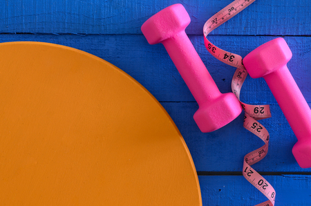 Dumbbells and tape measure on wooden background with copy space. Saturated colors (blue, orange, pink). Sport equipment. Active, healthy lifestyle conceptの写真素材