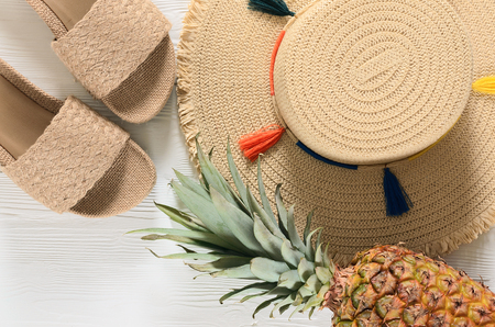 Womens summer accessories (straw hat, flip flops), pineapple on white wooden background. Fashion look, travel and summer concept. Flat lay. Natural organic stuffの写真素材