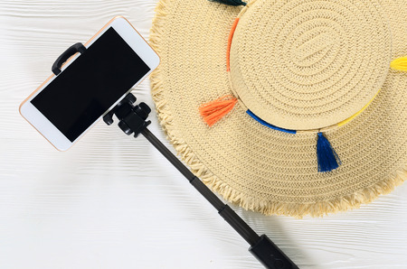 Womens summer accessories (straw hat, cellphone, selfie stick) on white wooden background with copy space. Fashion travel concept. Flat layの写真素材