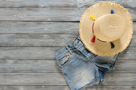 Womens clothing, accessories (denim shorts, straw hat) on grey wooden background with copy space. Trendy fashion outfit. Shopping concept. Mock up for online store.  Flat lay. Summer collection
の写真素材