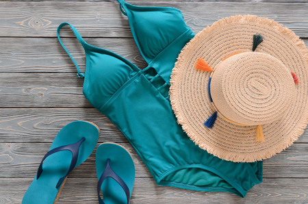 Womens clothing, accessories, shoes (straw hat, blue green swimsuit, flip flops) on grey wooden background. Trendy fashion outfit. Shopping, travel, summer, beach concept, abstract.  Flat layの写真素材