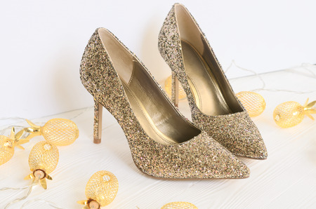 Womens gold chunky glitter pumps. Shoes for wedding, christmas, new year, evening, cocktail, night out. Golden stiletto heels. Flat lay. Footwear on white wooden background with copy spaceの写真素材