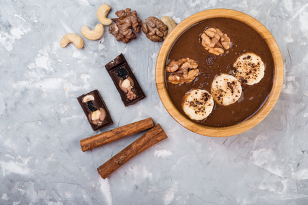 Chocolate smoothie on a wooden bowl with banana and nuts on grey  background, top viewの写真素材