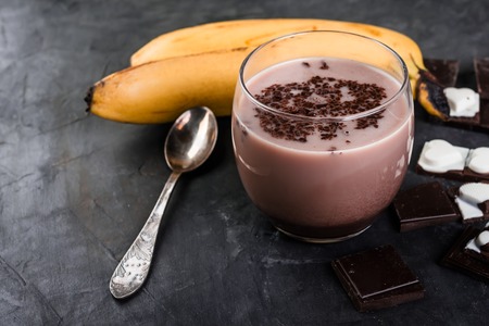 Glass of chocolate banana milkshake on dark  background, healthy breakfastの写真素材