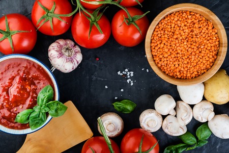 Lentil with tomatoes  sause and fresh  vegetables  for tasty cooking on  dark background. Top view.の写真素材