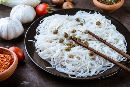 Rice noodles with vegetables, capers and soy sauce in the ceramic plate  on dark background.