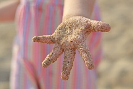 A small child plays with the sand, his palm is covered with sand and he shows his hands, summer vacations, childrens joy and happinessの写真素材