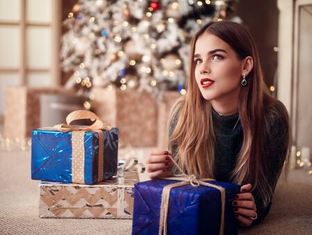 Smiling beautiful woman sitting at home near christmas treeの写真素材