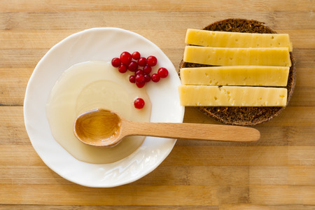 honey in a wooden spoon and cranberries on a white plate and a sandwich of black bread with cheeseの写真素材